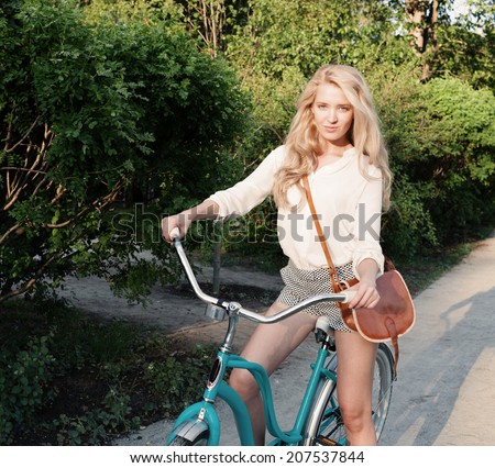 Young sexy blonde girl with long hair with brown vintage bag sits in a vintage bicycle