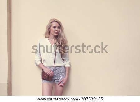 beautiful sexy blonde woman with long hair posing at the wall with vintage camera