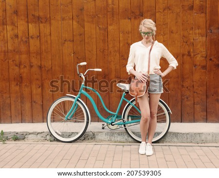 Young sexy blonde girl is standing near the vintage green bicycle with brown vintage bag in green sunglasses.