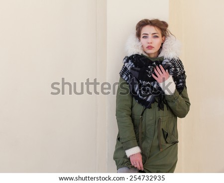 Beautiful unusual girl in a green jacket on background light wall