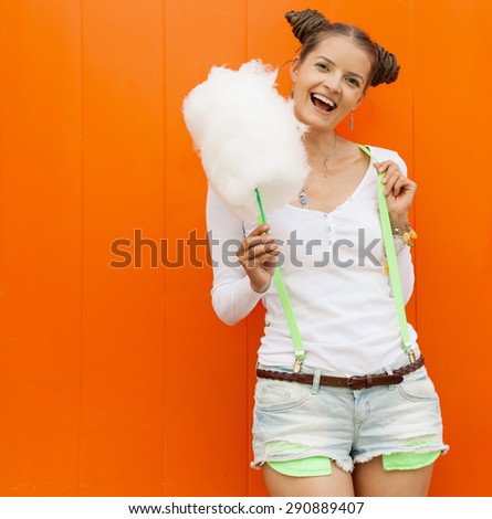 Beautiful fashionable girl with candy-floss posing next to the orange wall. Outdoor. Warm colors