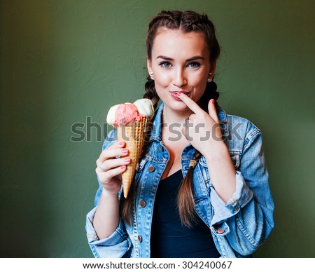 Beautiful girl with braids sitting in a cafe and eating huge multicolored ice cream in a waffle cone. Licking finger
