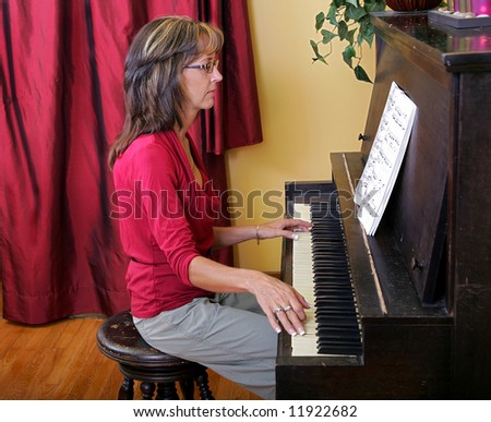 side view a women in red playing an upright piano