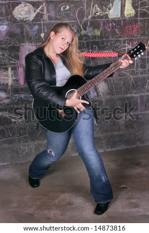 young moody adult female rocker jamming in front of a dark graffiti wall