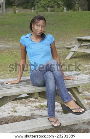 one African American young woman dressed in blue sitting on a picnic table in the park