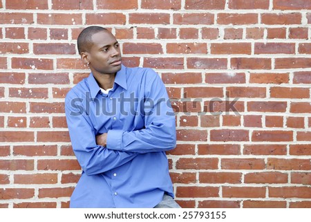 half length portrait of one African American man against a brick wall looking off camera outdoors