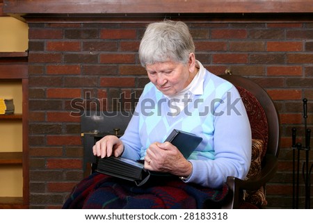 one elderly adult female sitting in a chair near the fireplace looking at a photo album