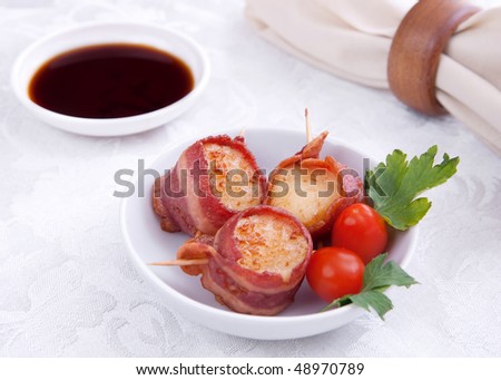 plate of three bacon wrapped scallops with cherry tomato garnish on a brown plate with sauce and napkin