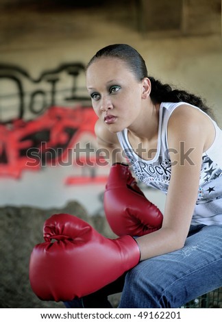 one young minority beautiful woman sitting outdoors in front of graffiti with boxing gloves on looking serious and ready to fight