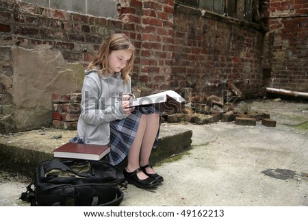 one young cute female student out of place in an old, run down brick warehouse district studying while alone