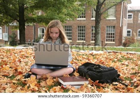 one young grade school student studying outdoors on a laptop in autumn