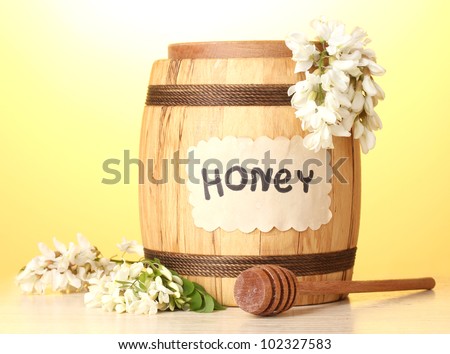 Sweet honey in barrel with acacia flowers on wooden table on yellow background
