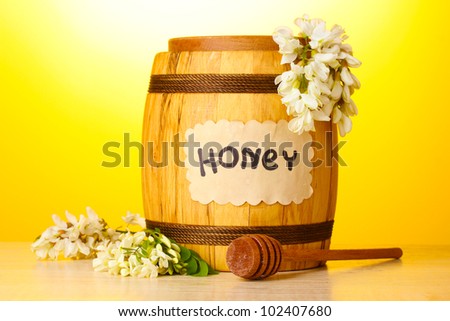 Sweet honey in barrel with acacia flowers on wooden table on yellow background