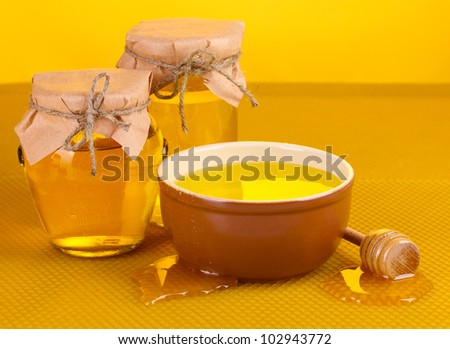 Jars of honey, bowl and wooden drizzler with honey on yellow honeycomb background