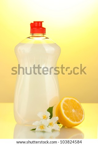 Dishwashing liquid, lemon and flowers on yellow background