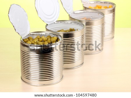 Open tin cans of peas, corn, bean and french bean on wooden table on green background