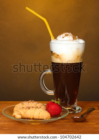 glass of coffee cocktail with croissants and strawberry on saucer on brown background