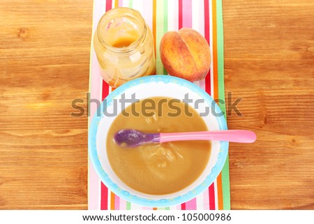 Peach baby food in a plate on colorful napkin on wooden table close-up