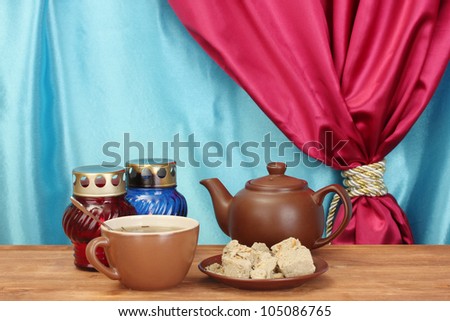 Teapot with cup and saucer with  sweet halva on wooden table on a background of curtain close-up