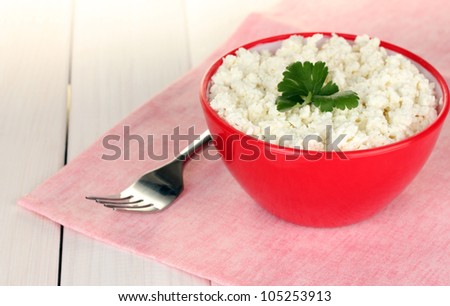 cottage cheese with parsley in red bowl and fork on pink napkin on white wooden table close-up