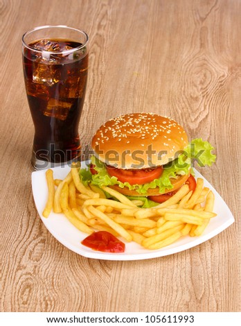 Big and tasty hamburger and fried potatoes on plate with cola on wooden table