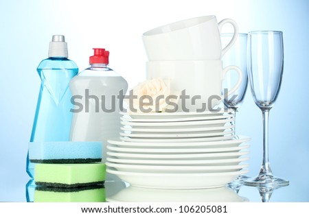 empty clean plates, glasses and cups with dishwashing liquid and sponges on blue background