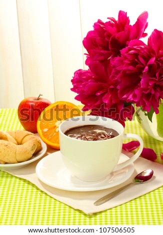 cup hot chocolate, apple, orange, cookies and flowers on table in cafe