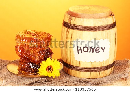 Barrel of honey and honeycomb on wooden table on orange background