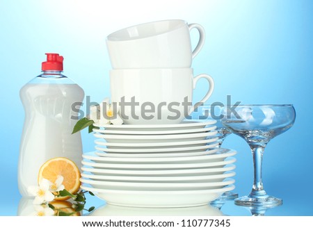 empty clean plates, glasses and cups with dishwashing liquid and lemon on blue background