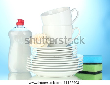empty clean plates and cups with dishwashing liquid and sponges on blue background