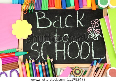 The words 'Back to School' written in chalk on the small school desk with various school supplies close-up