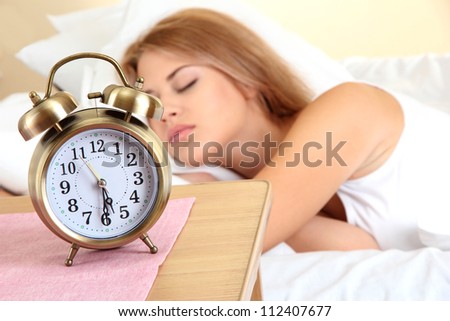 young beautiful woman sleeping on bed with alarm clock in bedroom