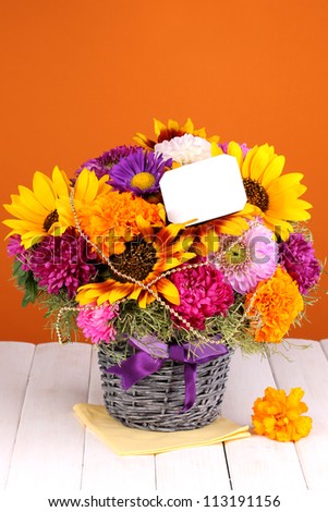 Beautiful bouquet of bright flowers with paper note on wooden table on orange background