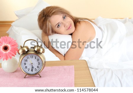 young beautiful woman lying on bed with alarm clock in bedroom