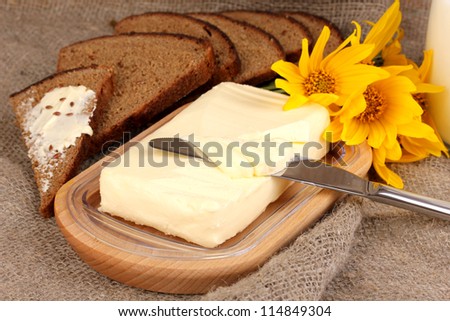 Butter on wooden holder surrounded by bread and flowers on sacking background