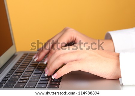 Hands typing on laptop keyboard close up on orange background