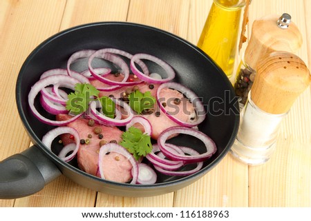 A pieces of pork with onions, spices and cooking oil fried in pan on wooden table