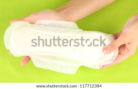 woman\'s hands holding a sanitary pad on green background close-up