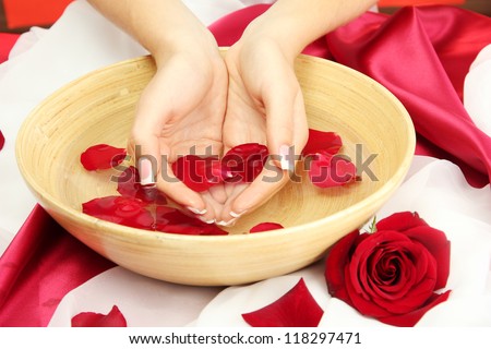 woman hands with wooden bowl of water with petals, on red background