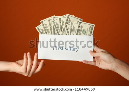 Woman\'s hand passes the envelope with the salary on brown background