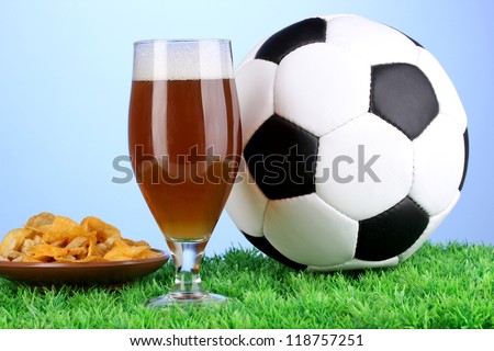 Glass of beer with soccer ball on grass on blue background