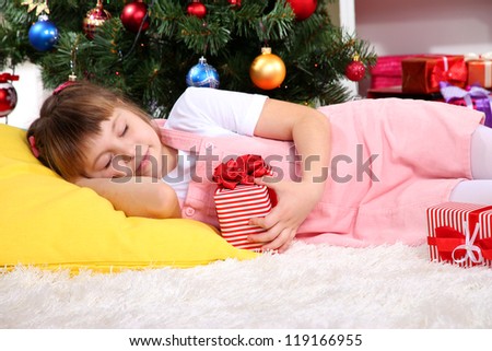 The little girl fell asleep with gift in their hands in festively decorated room