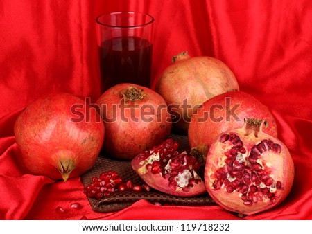 Ripe pomegranates with glass of pomegranate juice on red cloth background