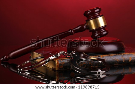 Gavel, handcuffs and book on law on red background