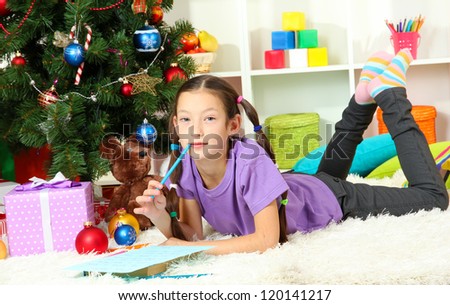 Little girl writing letter to Santa near christmas tree