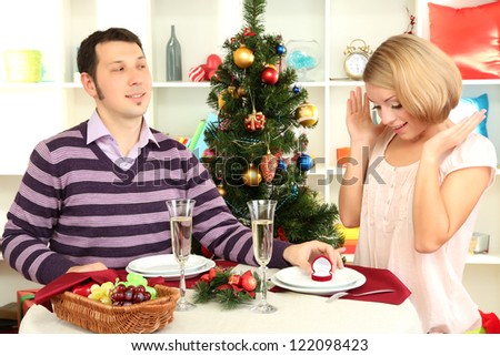 Young man makes proposal to marry girl at table near Christmas tree