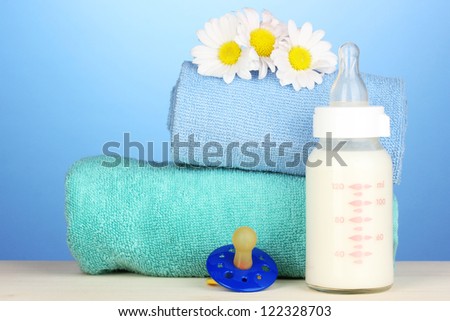 Baby bottle of milk with pacifier and towels on blue background