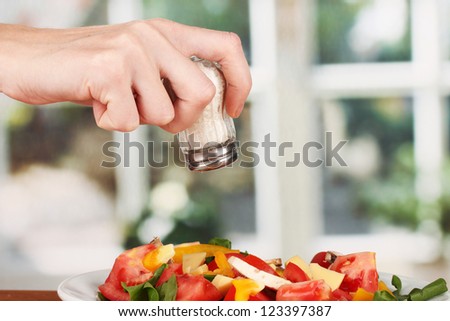 Hand adding salt using  salt shaker on bright background