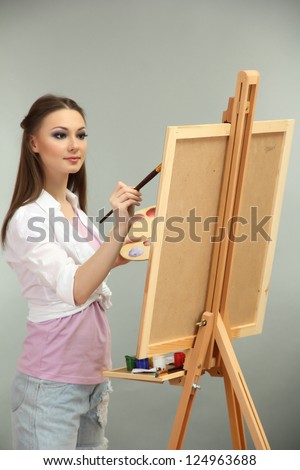 beautiful young woman painter at work, on grey background