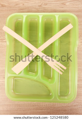 Green plastic cutlery tray with crossed wooden fork and scapula on wooden table